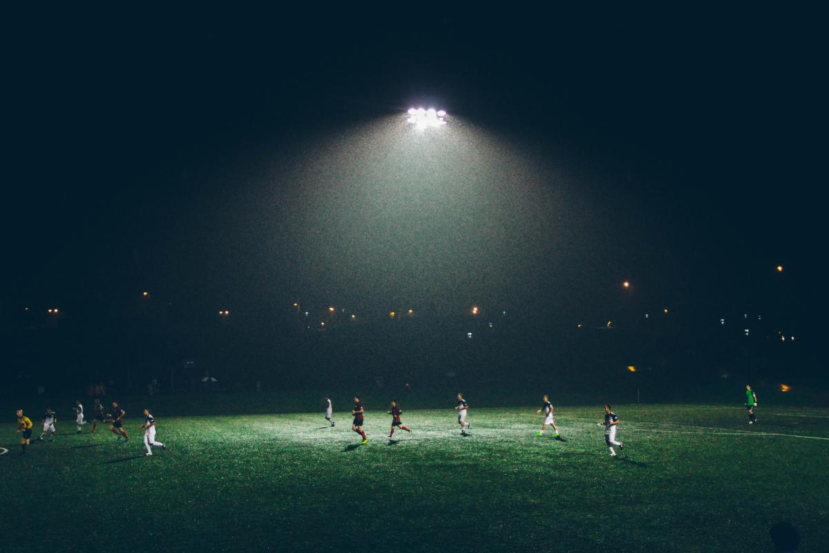 Voetballers in de avond, op een veld verlicht door lampen